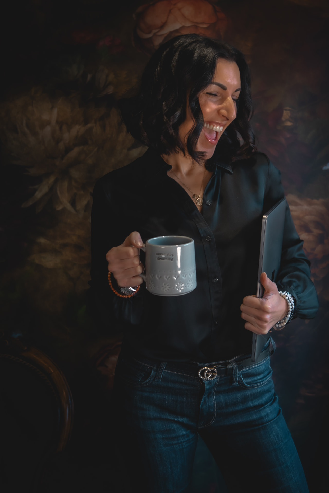 Naomi Buff laughing while holding a mug and laptop